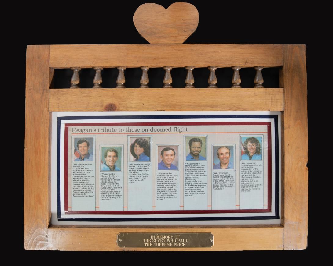 Challenger Plaque Artifact ID: 1986.10130.01 Object Name: Plaque Date Made: 1986 Description: A newspaper clipping title “Reagan’s tribute to those on doomed flight” with color photographs of each crew member of the Space Shuttle Challenger and a quote from President Reagan from his memorial speech. The newspaper is encapsulated in a wooden frame with a large heart at the top center. At the bottom center of the wooden frame is a small metal plaque engraved “IN MEMORY OF THE SEVEN WHO PAID THE SUPREME PRICE.
