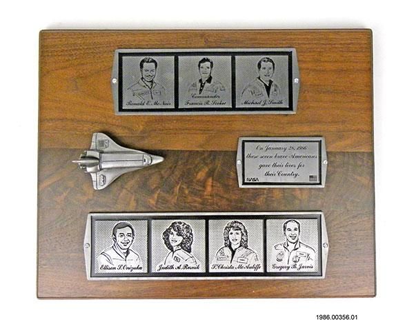 Challenger Plaque Artifact ID: 1986.00356.01 Object Name: Plaque Maker: Creative Products, Inc. Date: 1986 Description: A wooden plaque with three metal etched plates and a 3D sculpture of the Challenger spacecraft. The metal plates at the top and bottom of the plaque have metal etched images of the seven crew members along with their names. The plate on the right side states, "On January 28, 1986, these seven brave Americans gave their lives for their Country."